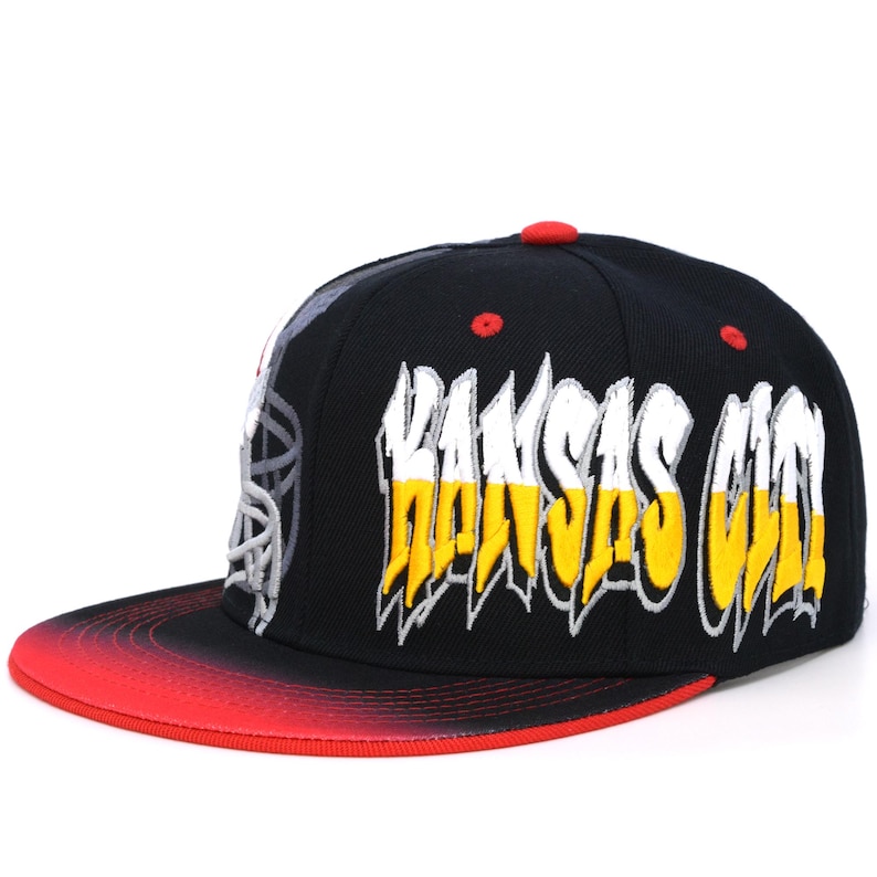 May include: Black and red baseball cap with a white and yellow "Kansas City" graphic on the front.