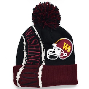 Op de afbeelding: Zwarte en bordeauxrode gebreide beanie met een pompon bovenop. De beanie heeft een wit streepontwerp en een Washington football helmlogo met de letter "W" aan de zijkant.
