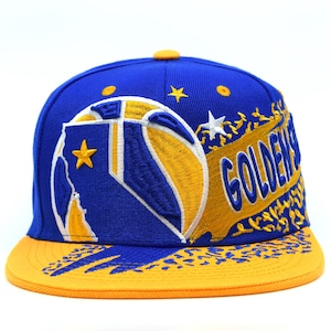 Könnte beinhalten: Eine blau-gelbe Baseballkappe mit dem Wort "GOLDEN" auf der Seite gestickt. Die Kappe hat ein Basketball-Design und Sternakzente. Der Schirm ist gelb und die Krone ist blau.