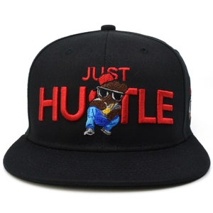 May include: Black baseball cap with a red embroidered "JUST HUSTLE" text and a cartoon character wearing sunglasses and a gold chain.