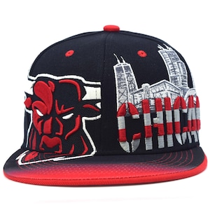 Puede incluir: Una gorra de béisbol negra con una gran cabeza de toro bordada en rojo y blanco en el lado izquierdo y un gráfico detallado de la silueta de Chicago bordado en blanco con la palabra CHICAGO en letras rojas y blancas a la derecha, visera roja.