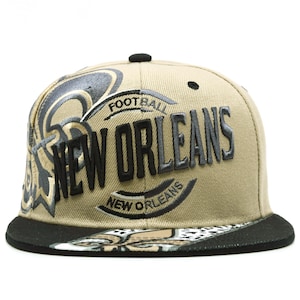 Op de afbeelding: Een beige honkbalpet met een zwarte klep en de geborduurde tekst NEW ORLEANS in het zwart. De pet heeft een zwart-beige fleur-de-lis afbeelding op de klep en een gestileerd football-logo aan de zijkant met het woord FOOTBALL boven de tekst.