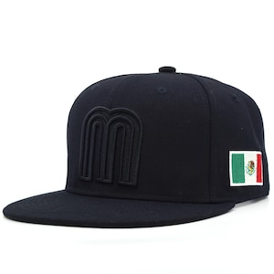 May include: A solid black baseball cap featuring a raised, tonal black letter M embroidered on the front panel. The side of the cap displays a rectangular patch with the green, white, and red vertical stripes of the Mexican flag and its central emblem.