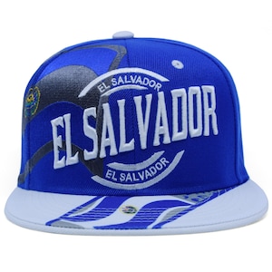 Può includere: Cappellino da baseball blu con la scritta "EL SALVADOR" a grandi lettere bianche. Il cappellino ha una visiera bianca e un disegno con le parole "EL SALVADOR" in un banner curvo. Bottone in alto.