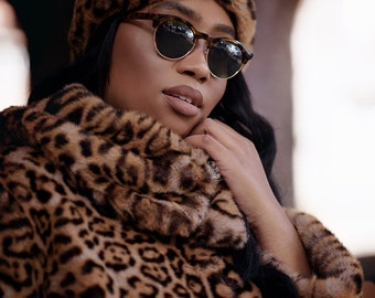 Puede incluir: Una mujer con un abrigo y un gorro de piel de leopardo con gafas redondas.