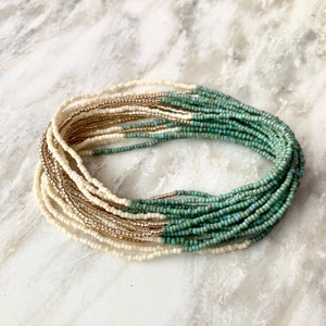 Op de afbeelding: Een meerstrengs kralenketting met een verloop van witte en turquoise kralen.