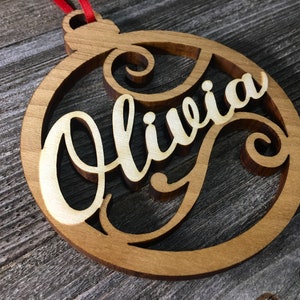 May include: A wooden Christmas ornament in the shape of a circle with the name "Olivia" cut out in a decorative script font.