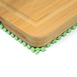 May include: A close-up of a wooden cutting board with a green non-slip mat underneath. The cutting board is made of light brown bamboo and has a rounded edge.