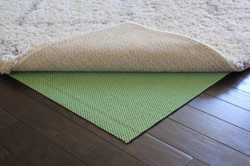 K&ouml;nnte beinhalten: Ein gr&uuml;ner Unterleger f&uuml;r Teppiche liegt unter einem wei&szlig;en Teppich. Der Unterleger ist so konzipiert, dass der Teppich nicht auf dem Holzboden rutscht.