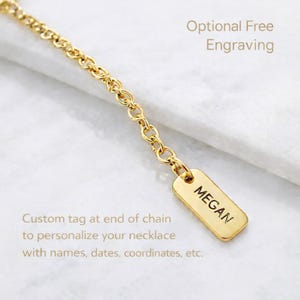 May include: A gold-toned metal chain featuring a small, rectangular pendant tag at the end. The tag is engraved with the name MEGAN in black capital letters. The text Optional Free Engraving and Custom tag at end of chain to personalise your necklace with names, dates, coordinates, etc. is visible.