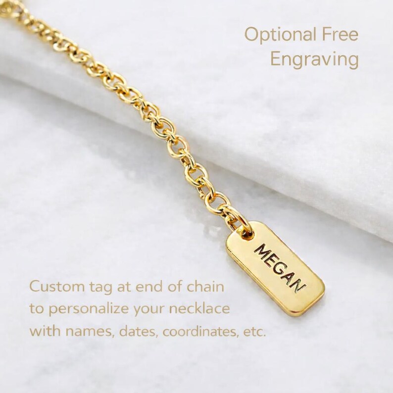 May include: A gold-toned metal chain featuring a small, rectangular pendant tag at the end. The tag is engraved with the name MEGAN in black capital letters. The text Optional Free Engraving and Custom tag at end of chain to personalise your necklace with names, dates, coordinates, etc. is visible.