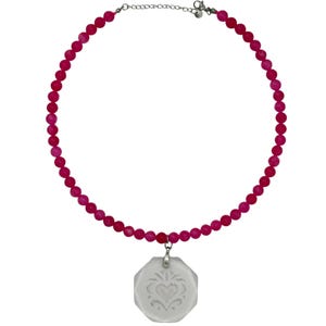 May include: A necklace featuring a strand of small, round, vibrant pink beads. The necklace includes a silver-toned metal chain extender with a lobster clasp. A single, octagonal, translucent white pendant with an etched heart design hangs centrally.