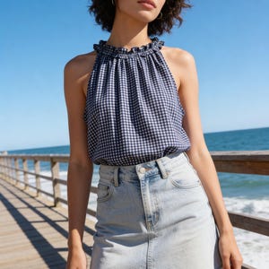 Pu&ograve; includere: Un top halter a quadretti blu navy e bianco con scollatura arricciata e una gonna di jeans azzurra. La gonna ha un orlo grezzo. L'outfit &egrave; indossato all'aperto vicino al mare.