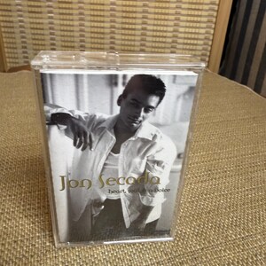 May include: A black and white cassette tape featuring Jon Secada. The album cover shows a portrait of the artist in a white shirt. The album title "heart, soul & voice" is visible.