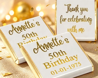 May include: Three square chocolate bars wrapped in white foil with gold metallic text. Two bars read Annette's 50th Birthday with the date 01-01-1975, while the third bar reads Thank you for celebrating with me in elegant gold script lettering.