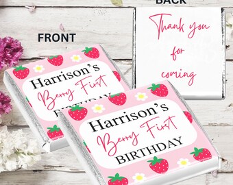 May include: Two pink and white chocolate bar wrappers with a strawberry pattern. The front of the wrapper says "Harrison's Berry First Birthday". The back of the wrapper says "Thank you for coming".