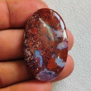 Könnte beinhalten: Ovaler Cabochon-Edelstein mit einem braunen, weißen und violetten Achatmuster. Der Stein hat eine polierte, glatte Oberfläche.