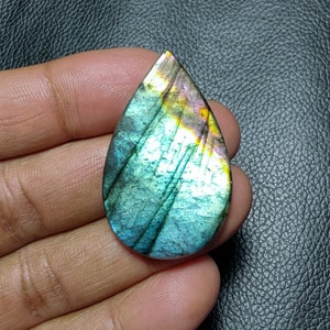 Könnte beinhalten: Ein tropfenförmiger Labradorit-Cabochon mit schillernden blauen, grünen und goldenen Farben.