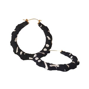 May include: A pair of large hoop earrings. The hoops are wrapped in black fabric with a white polka dot pattern. The earring posts are gold-colored.