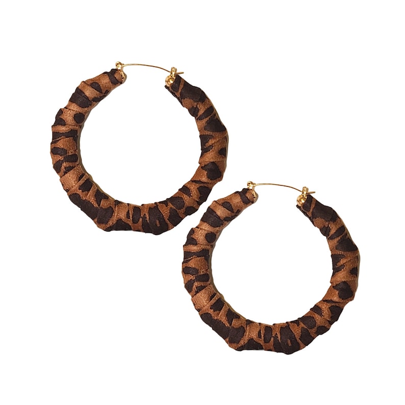 May include: A pair of hoop earrings with a brown and black animal print design. The hoops are wrapped in fabric with a gold-colored clasp.