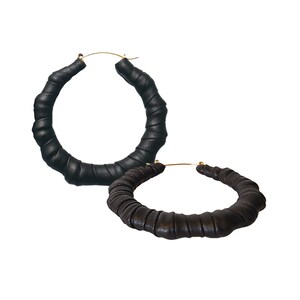 May include: A pair of large black leather hoop earrings. The earrings are made of thick, braided leather and have a gold-tone closure.