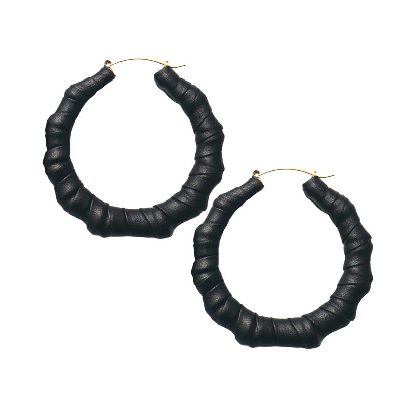 May include: A pair of large black hoop earrings with a twisted leather design. The earrings are made of a thick, durable material and have a gold-tone finish.