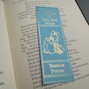 May include: A blue bookmark with gold lettering and a mouse illustration. The bookmark features the title "The Tale of Two Bad Mice" and the author "Beatrix Potter".