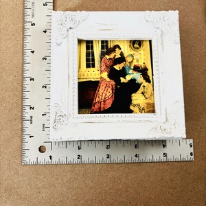 Puede incluir: Un marco de fotos blanco con un dise&ntilde;o decorativo ornamentado. El marco contiene una impresi&oacute;n vintage de un grupo de personas en una habitaci&oacute;n. La impresi&oacute;n est&aacute; en tonos c&aacute;lidos de amarillo, naranja y rojo.