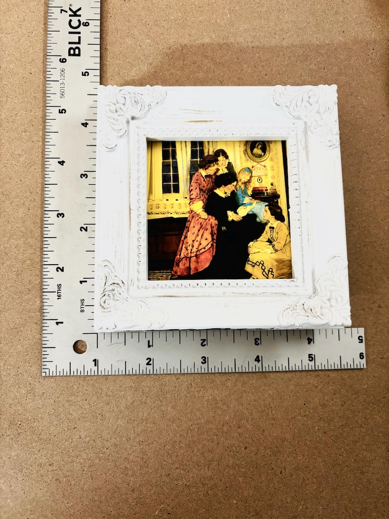 Puede incluir: Un marco de fotos blanco con un dise&ntilde;o decorativo ornamentado. El marco contiene una impresi&oacute;n vintage de un grupo de personas en una habitaci&oacute;n. La impresi&oacute;n est&aacute; en tonos c&aacute;lidos de amarillo, naranja y rojo.
