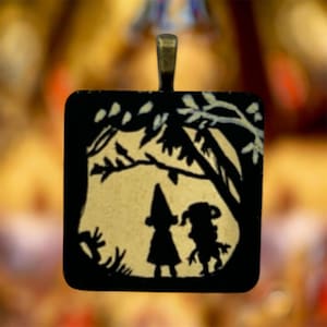 May include: A square pendant featuring a black silhouette design on a cream background. The image depicts two figures standing under tree branches. The pendant has a dark metal bail at the top for attachment to a chain or cord.