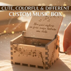 Puede incluir: Una caja de música personalizada de madera con notas musicales y el texto "Non puoi cogliere un fiore senza turbare una stella." La caja está abierta, revelando el mecanismo interno, y tiene una manivela.
