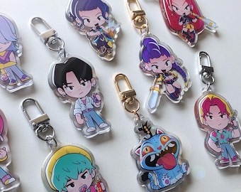 May include: A collection of clear acrylic keychains featuring colorful cartoon character designs. Each keychain has a silver or gold-colored clasp. The characters have various hairstyles and outfits, with some holding objects like bottles or weapons.