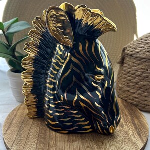 May include: Black and gold zebra head sculpture. The zebra has a black and gold striped pattern and a gold mane. The sculpture is made of ceramic and has a glossy finish.