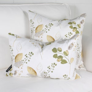 May include: Two decorative throw pillows with a botanical leaf pattern. The pillows feature a white background with a repeating design of green, gold, and gray leaves and berries. The pillows are rectangular and square.