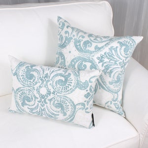 May include: Two decorative throw pillows with a white background and a blue damask pattern. The pillows are on a white couch.