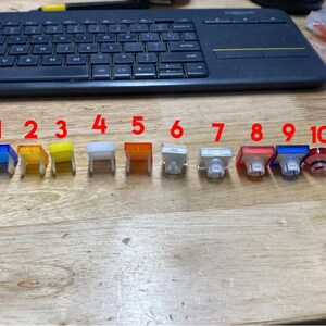Pu&ograve; includere: Dieci tasti in plastica di diversi colori, numerati da 1 a 10, disposti in fila su una superficie di legno.