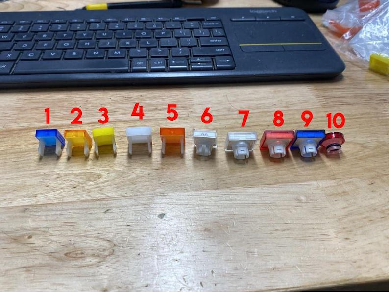 Pu&ograve; includere: Dieci tasti in plastica di diversi colori, numerati da 1 a 10, disposti in fila su una superficie di legno.
