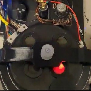 May include: Close-up of a black and silver circular device with a red light. The device has a black strap and a silver knob.