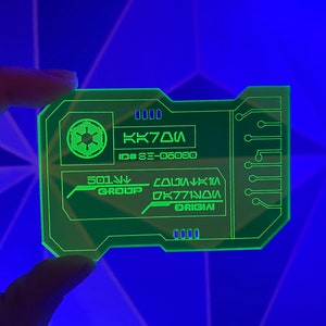 Puede incluir: Una tarjeta de pl&aacute;stico verde con un s&iacute;mbolo imperial de Star Wars, el texto "KK70A", "ID# 3E-06090", "501st GROUP", "COLUMBIA", "DK771N0A" y "ORIGIN".