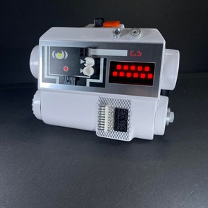 May include: A white plastic device with a red digital display and a black and white control panel. The device has a black and white label with the text "C3" on it.