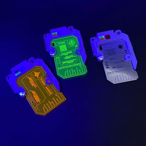 May include: Three glow-in-the-dark keychains with circuit board designs. The keychains are blue, green, and orange. The text on the keychains reads "77MO", "INVICTUS", and "DOMINICUS".