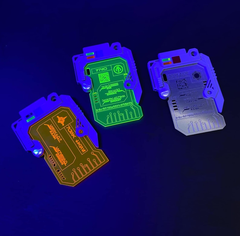 May include: Three glow-in-the-dark keychains with circuit board designs. The keychains are blue, green, and orange. The text on the keychains reads "77MO", "INVICTUS", and "DOMINICUS".