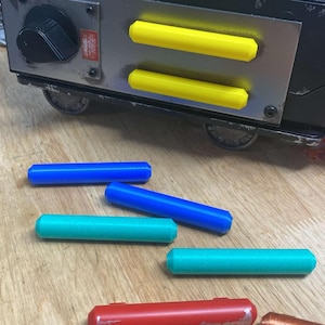 May include: Four colorful plastic rods, two blue, two green, lying on a wooden surface. The rods are about 10 inches long and 1 inch in diameter.  The rods are arranged in a random pattern.  There is a black and yellow object in the background.