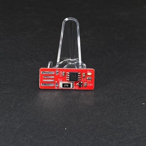 Può includere: Una scheda di circuito rosso con vari componenti elettronici, tra cui resistori, condensatori e un piccolo circuito integrato. La scheda ha etichette di testo tra cui "R1", "R2", "C1", "C2", "PD", "POR" e "270".