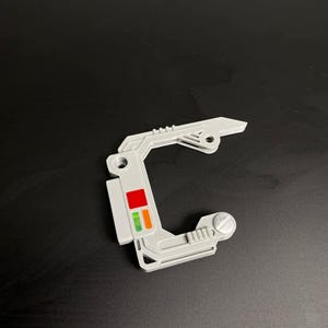 May include: A white plastic part with a red, orange, and green light indicator. The part has a screw on the right side and a small hole on the left side.