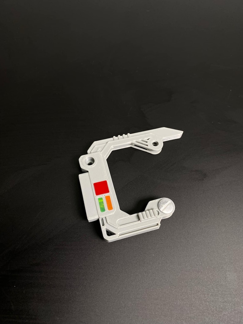 May include: A white plastic part with a red, orange, and green light indicator. The part has a screw on the right side and a small hole on the left side.