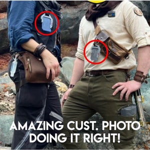 May include: Two people wearing brown leather belts with silver buckles and gray rectangular pouches attached to the belts. The pouches are attached to the belts with black straps. The people are wearing casual clothing. The text "AMAZING CUST. PHOTO DOING IT RIGHT!" is at the bottom of the image.