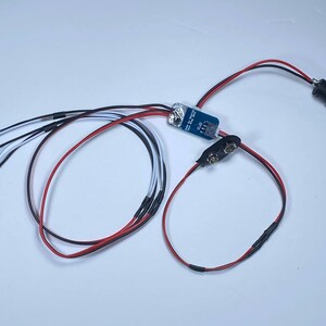 K&ouml;nnte beinhalten: Eine kleine Platine mit Dr&auml;hten, die mit einem Batteriepack und einem Schalter verbunden sind. Au&szlig;erdem sind f&uuml;nf wei&szlig;e LED-Leuchten an die Platine angeschlossen.