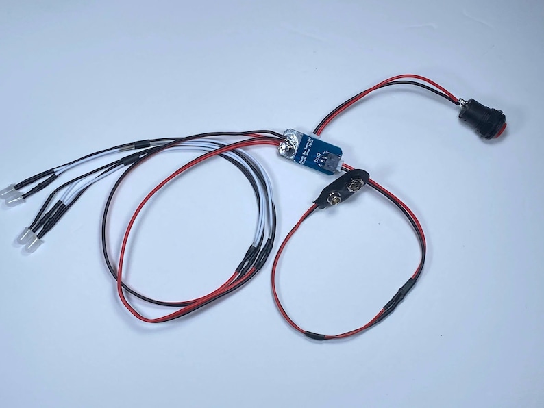 K&ouml;nnte beinhalten: Eine kleine Platine mit Dr&auml;hten, die mit einem Batteriepack und einem Schalter verbunden sind. Au&szlig;erdem sind f&uuml;nf wei&szlig;e LED-Leuchten an die Platine angeschlossen.