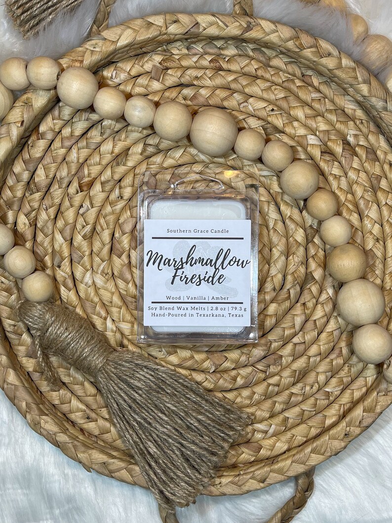 Puede incluir: Un derretido de cera blanco con el texto "Southern Grace Candle Marshmallow Fireside Wood | Vanilla | Amber Soy Blend Wax Melts | 2.8 oz | 79.3 g Hand-Poured in Texarkana, Texas" en la etiqueta. El derretido de cera est&aacute; sentado en una cesta tejida.